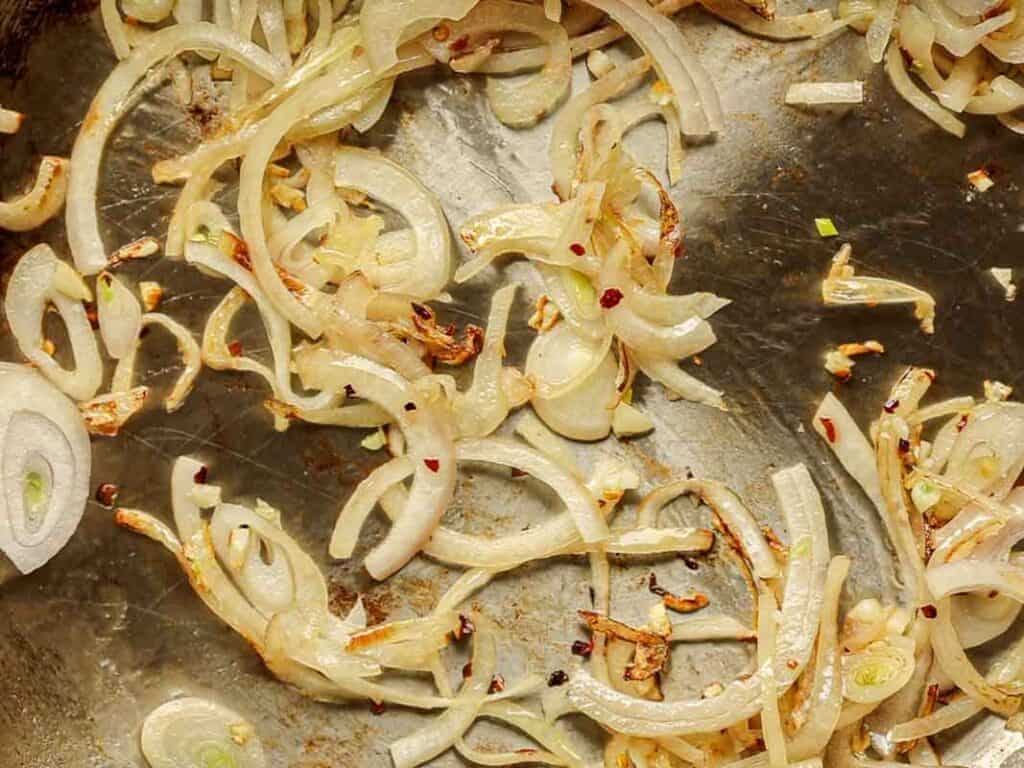 Close-up of julienned shallots and garlic being sautéed in a pan.